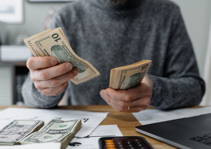 A landlord in a grey sweater counts their rent money in american money at a desk.